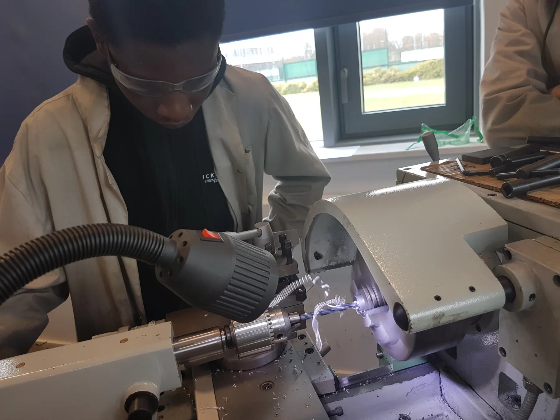 Fhaeeq turning a part on a centre lathe, wearing safety glasses